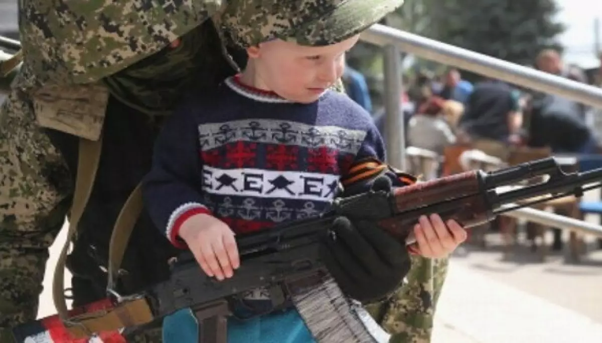 Хлопчик тримає автомат під наглядом солдата під час мілітаризації дітей