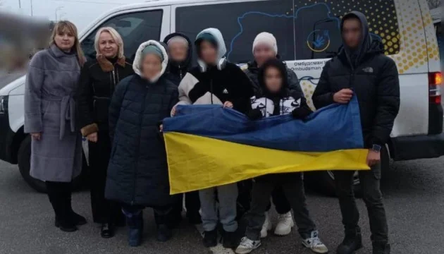 Дети, возвращенные из оккупации, держат флаг Украины возле фургона омбудсмена